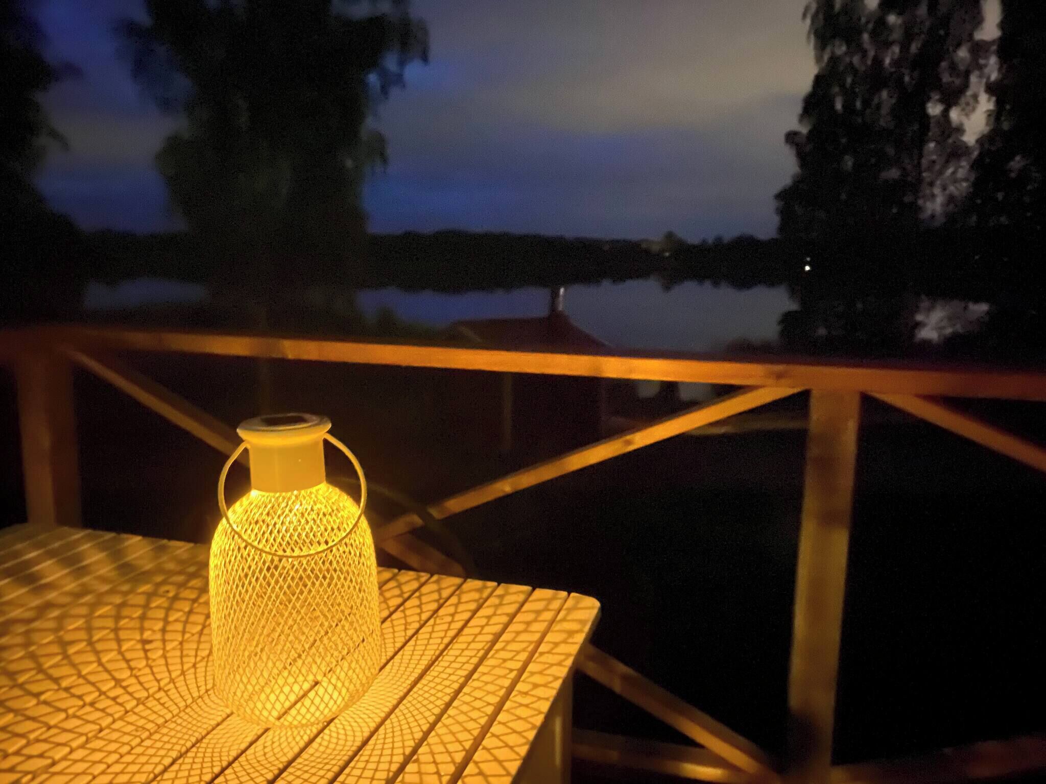 A table with a yellow mesh lantern on it, overlooking a body of water at dusk.