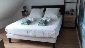 A neatly made bed with white linens and green towels, a bedside table with a lamp, and a wooden nightstand. - Room with outdoor spa unlimited access (Porcaro)