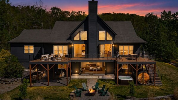 Ein zweistöckiges Haus mit überdachter Terrasse, Sitzgelegenheiten im Freien und einem Whirlpool.