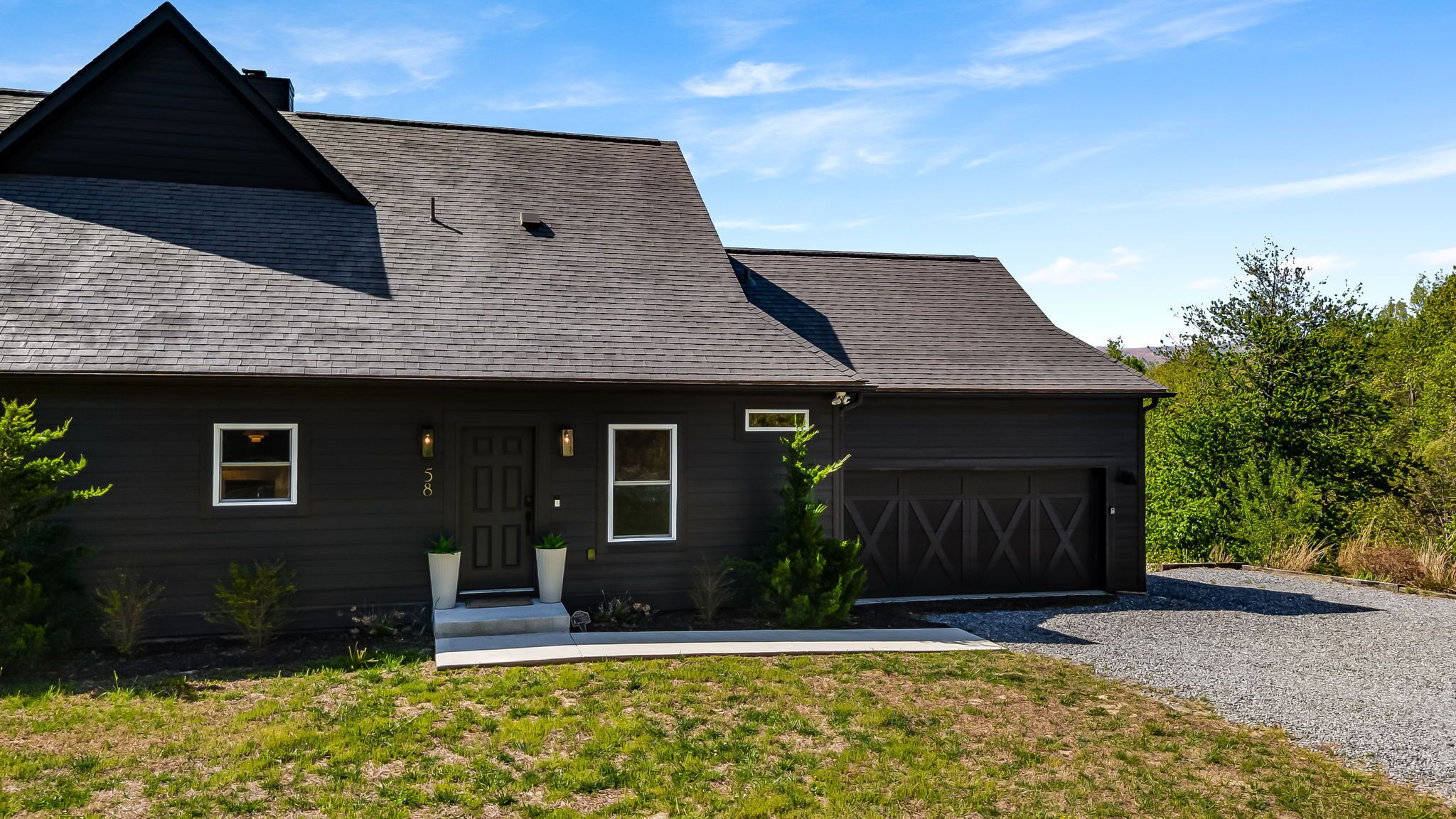 En mørk enfamiliehuset med saddeltag, garage og en indgangsport med plantekrukker.