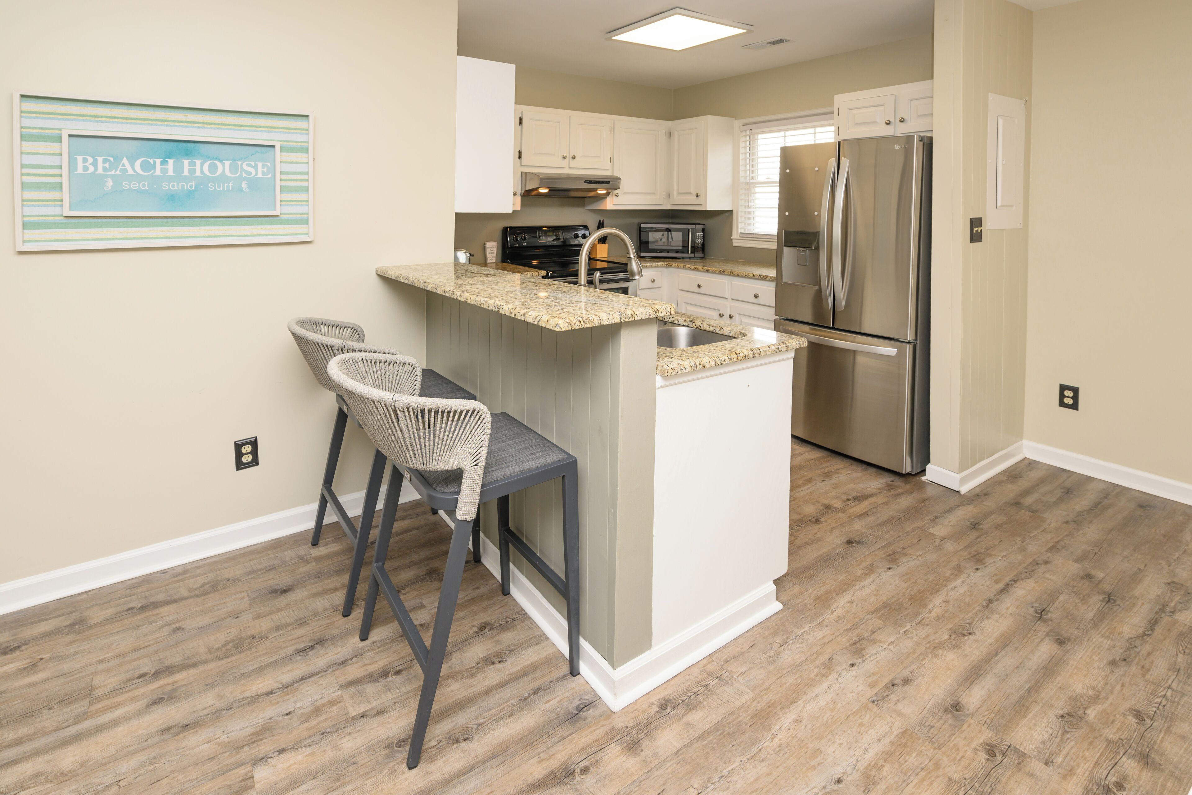 A kitchen with a central island, two bar stools, a stainless steel refrigerator, and a microwave.