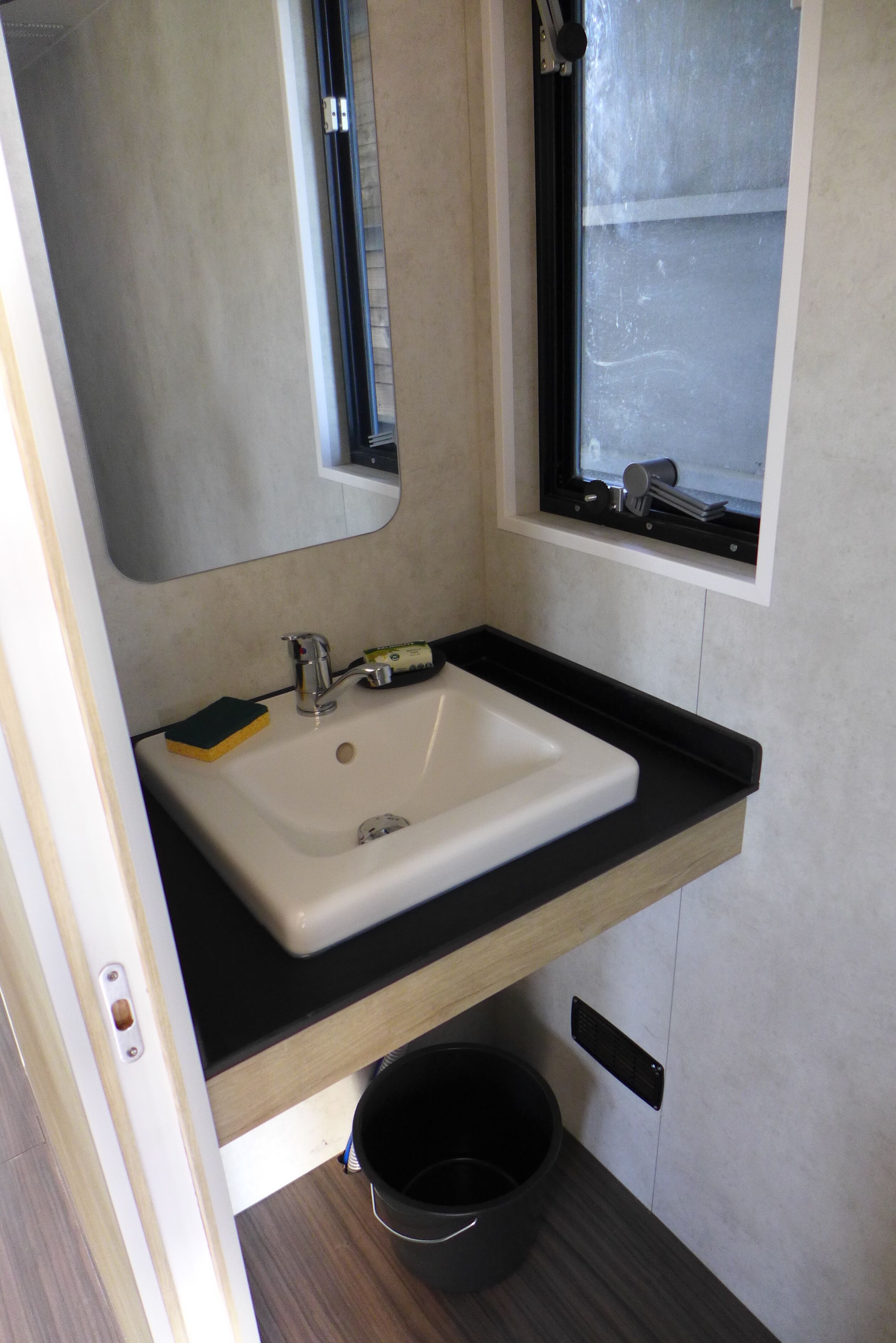 Un baño con un lavabo blanco, un espejo y una ventana.