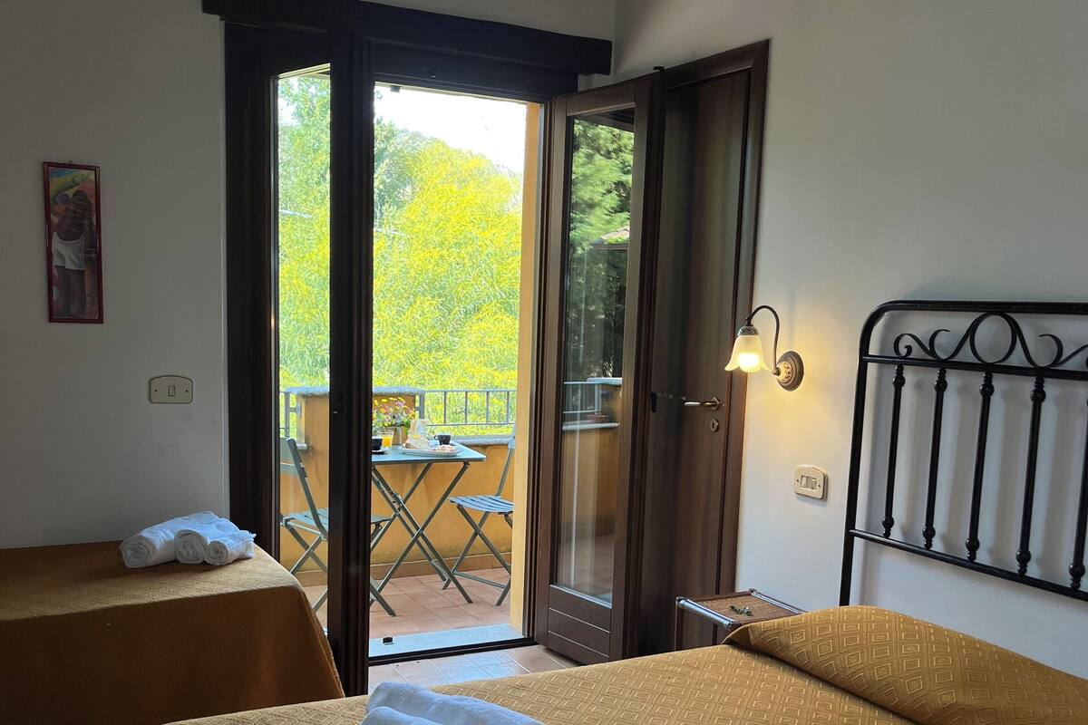 Ein Hotelzimmer mit zwei Betten, einem Balkon und Blick auf Grünflächen.