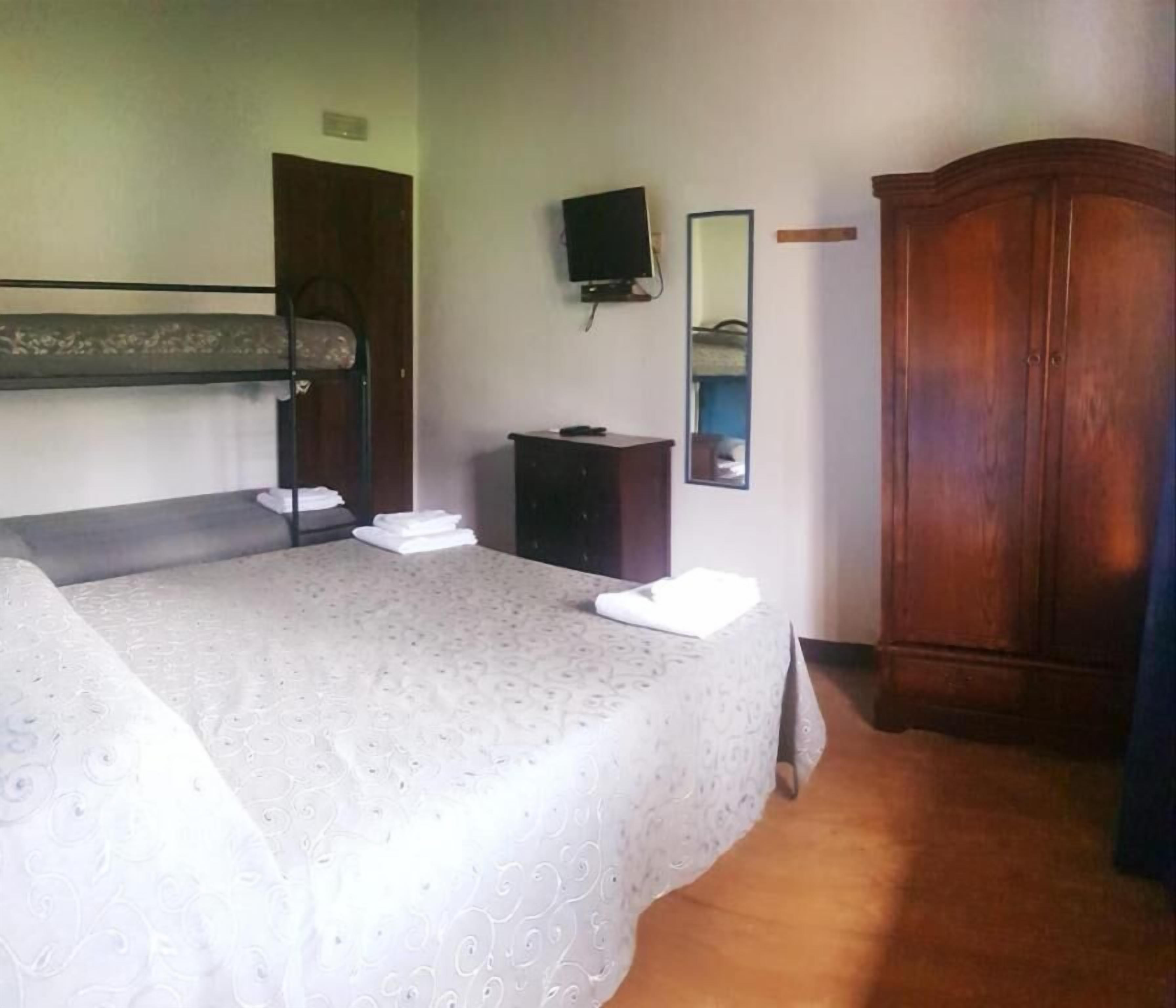 Una habitación con una cama litera, un armario de madera, un mueble pequeño, un televisor y un espejo en la pared.