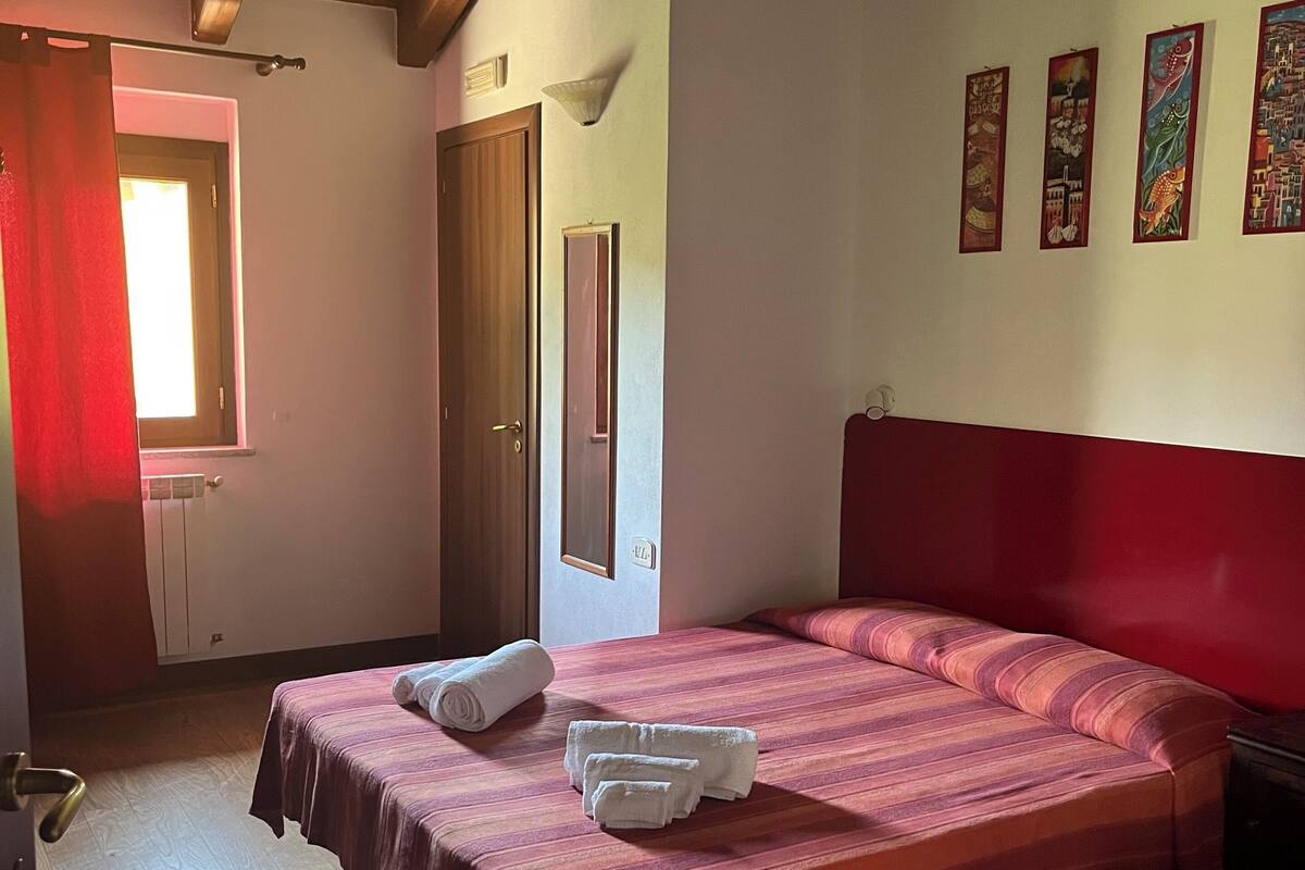 Ein Hotelzimmer mit zwei Betten, Holzboden, einem roten Kopfteil und einem Fenster mit roten Vorhängen.