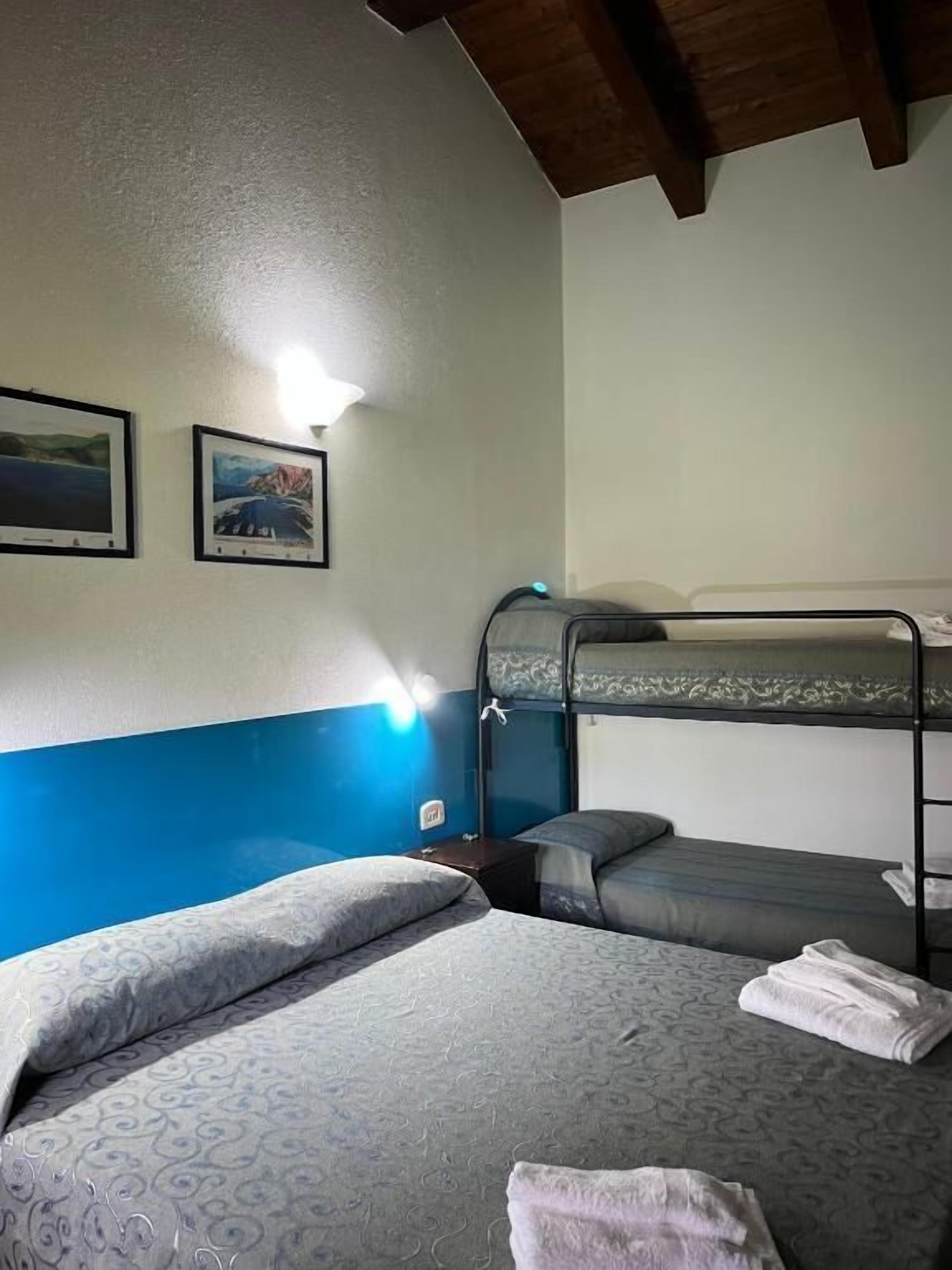 A room with bunk beds and a single bed, a wall-mounted lamp, and two framed pictures.