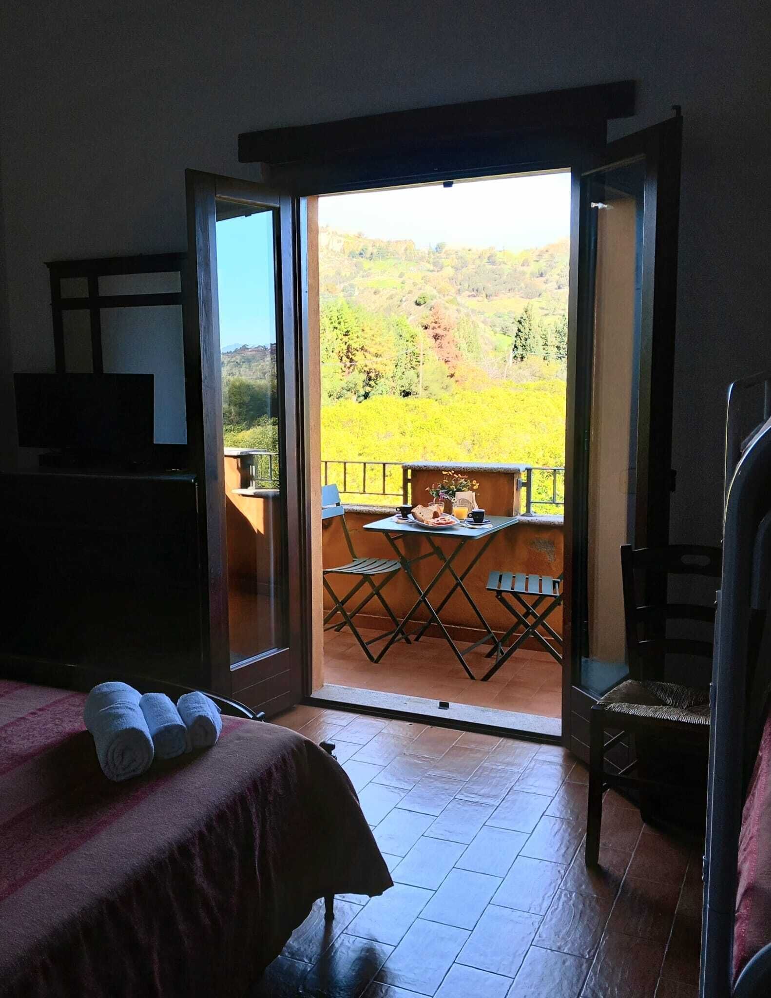A room with a bed, a table with chairs, and a balcony with a table and chairs.