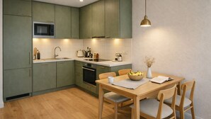 Cozinha moderna com armários verdes, micro-ondas, pia e área de jantar com mesa e cadeiras.