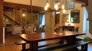 Una mesa de madera con bancos, focos colgantes, una escalera y sillas de mimbre blanco.