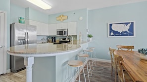 A kitchen with a central island, bar stools, a wooden dining table, and a map on the wall. - Shores of Panama #2228, 3BR+Bunk, Beachfront (Panama City Beach)