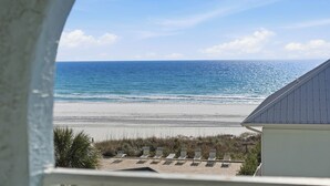 Vue sur la plage depuis un balcon, avec des chaises longues et un bâtiment au premier plan.