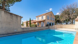 A swimming pool with a clear blue water surface, surrounded by a low wall and a building with a tiled roof and windows. - Château Mazane – Mas in the Heart of Vineyards, Pool and Mountain View (Sarrians)