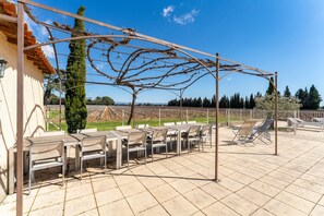 Un patio al aire libre con mesas y sillas, una pérgola cubierta de hiedra y vistas al campo.