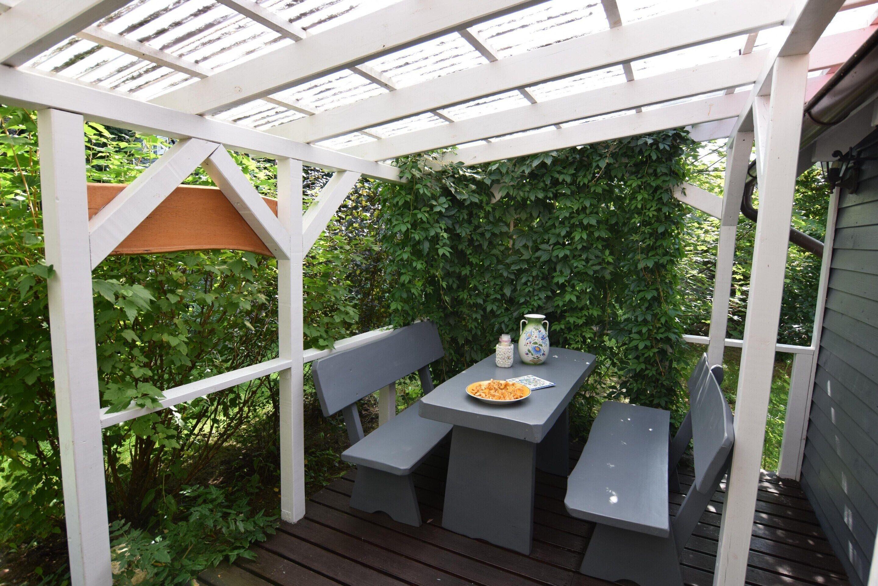 Un patio coperto con tavolo e panche, immerso nel verde.