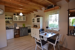 A kitchen with wooden beams, a dining table with chairs, a window with lace curtains, and a small refrigerator. - Comfortable Holiday Homes With a Beautiful Garden (Parchowo)