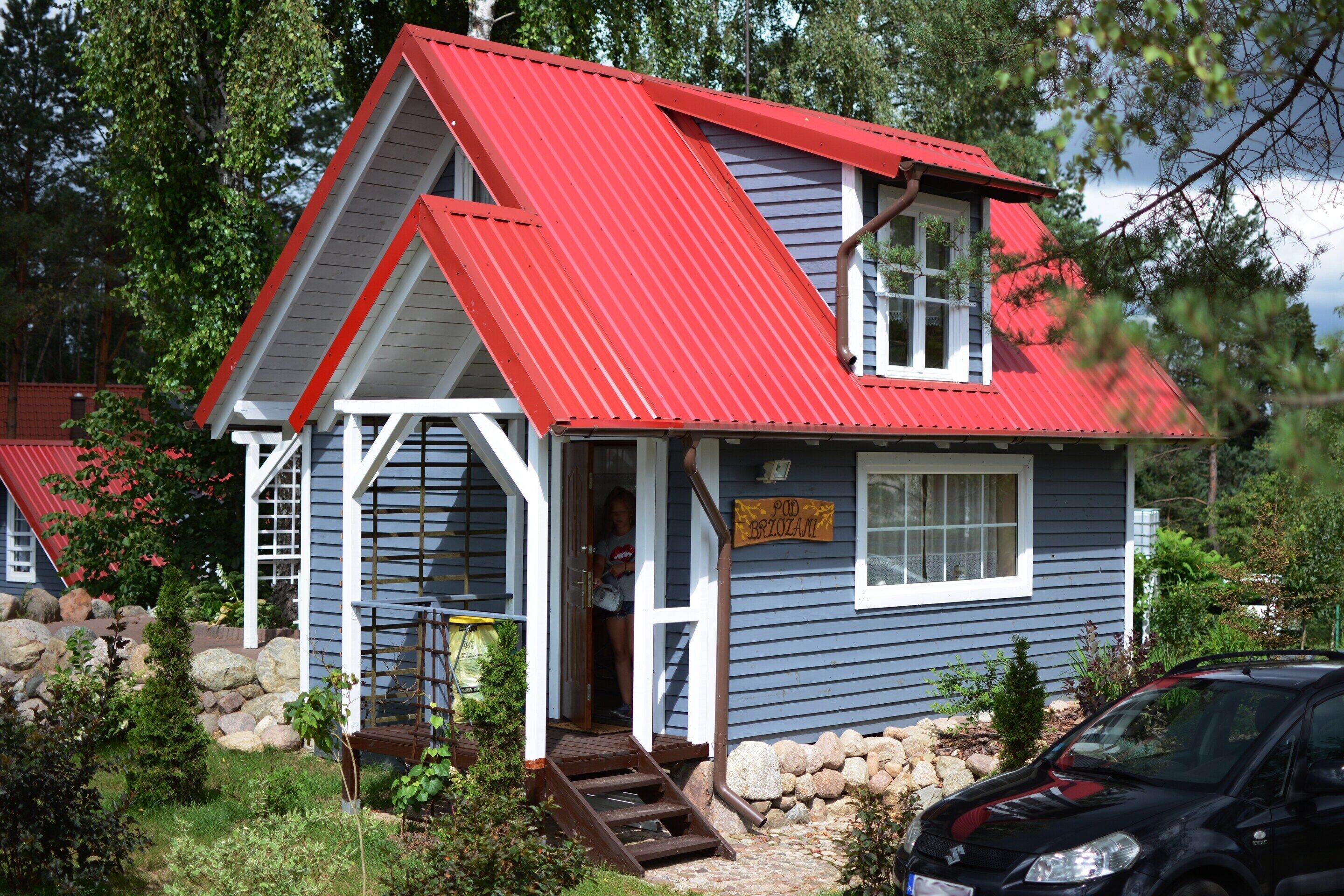 A two-story house with a red roof and a wooden staircase leading to the front door.
