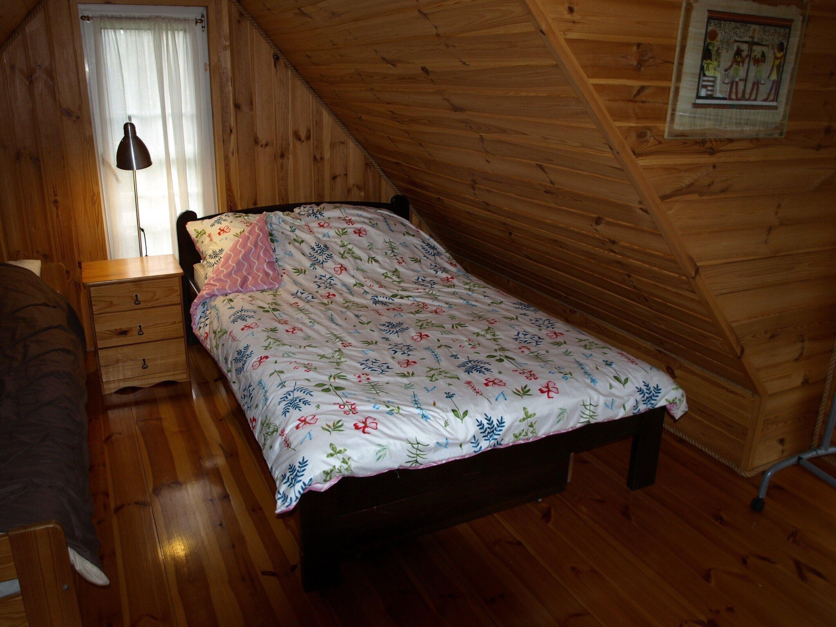 Una habitación pequeña con paneles de madera, una cama individual, una mesita de noche, una lámpara y una ventana con cortinas.