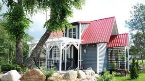 A house with a red roof, a porch with chairs, and a stone wall in the foreground. - Comfortable Holiday Homes With a Beautiful Garden (Parchowo)