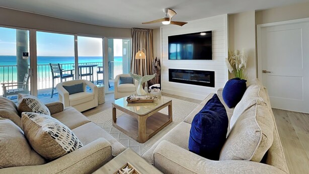 Una sala de estar con un televisor grande, asientos cómodos, una chimenea y vistas al océano.