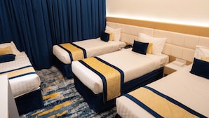 Ein Hotelzimmer mit drei Betten, jeweils mit einer blau-goldenen Tagesdecke, einem Kopfteil und einem Nachttisch.