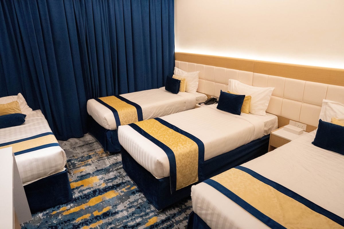 Ein Hotelzimmer mit drei Betten, jeweils mit einer blau-goldenen Tagesdecke, einem Kopfteil und einem Nachttisch.