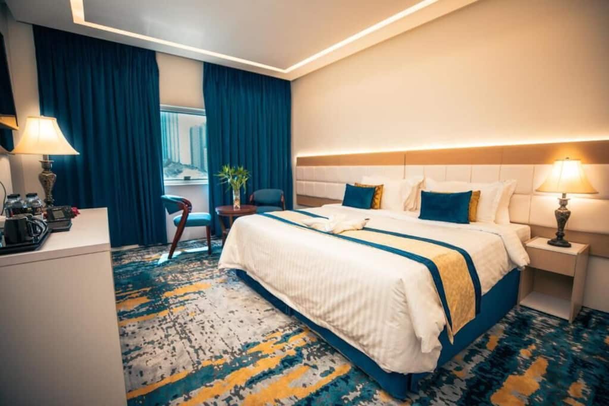 Ein Hotelzimmer mit einem großen Bett, einem Schreibtisch, einem Sessel, einem Nachttisch und einem Fenster mit Vorhängen.