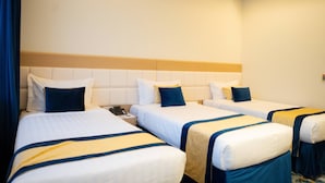 Ein Hotelzimmer mit drei Betten, jedes mit weißer Bettwäsche und blauen und gelben Akzenten.