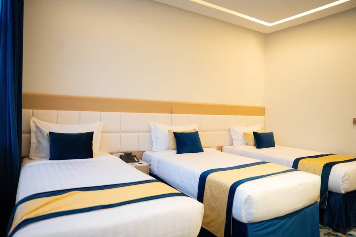 Ein Hotelzimmer mit drei Betten, jedes mit weißer Bettwäsche und blauen und gelben Akzenten.