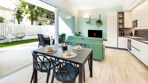 Une cuisine moderne avec un coin repas, un canapé vert et un téléviseur fixé au mur.