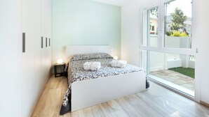 Une chambre moderne avec un grand lit, des lampes de chevet et une vue sur un jardin, accessible par une porte-fenêtre coulissante.