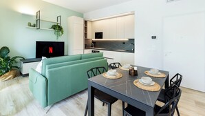 Un salon moderne avec un canapé vert, une table à manger dressée et un coin cuisine doté de meubles blancs et d’un plan de travail noir.