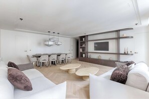 A modern living room with a sofa set, a dining table with chairs, a coffee table, a TV mounted on a wall, and built-in shelving. - Luxury Apartment Sentier Montorgueil I (Paris)
