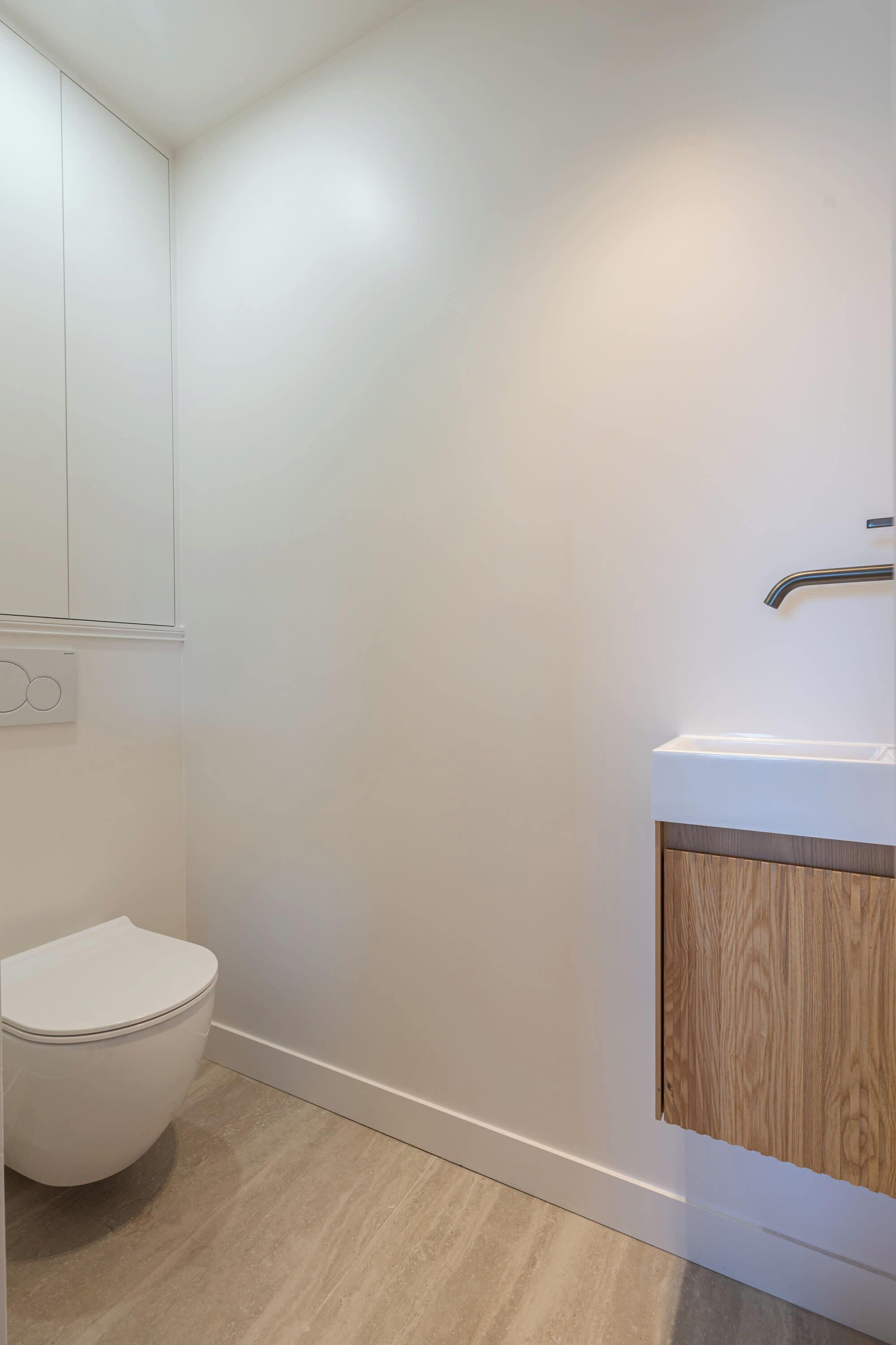 A bathroom with a white toilet, a wooden cabinet, and a white sink.