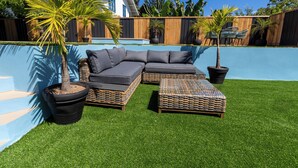 Ein Garten mit Pool, Ecksofa und Kübelpflanzen.