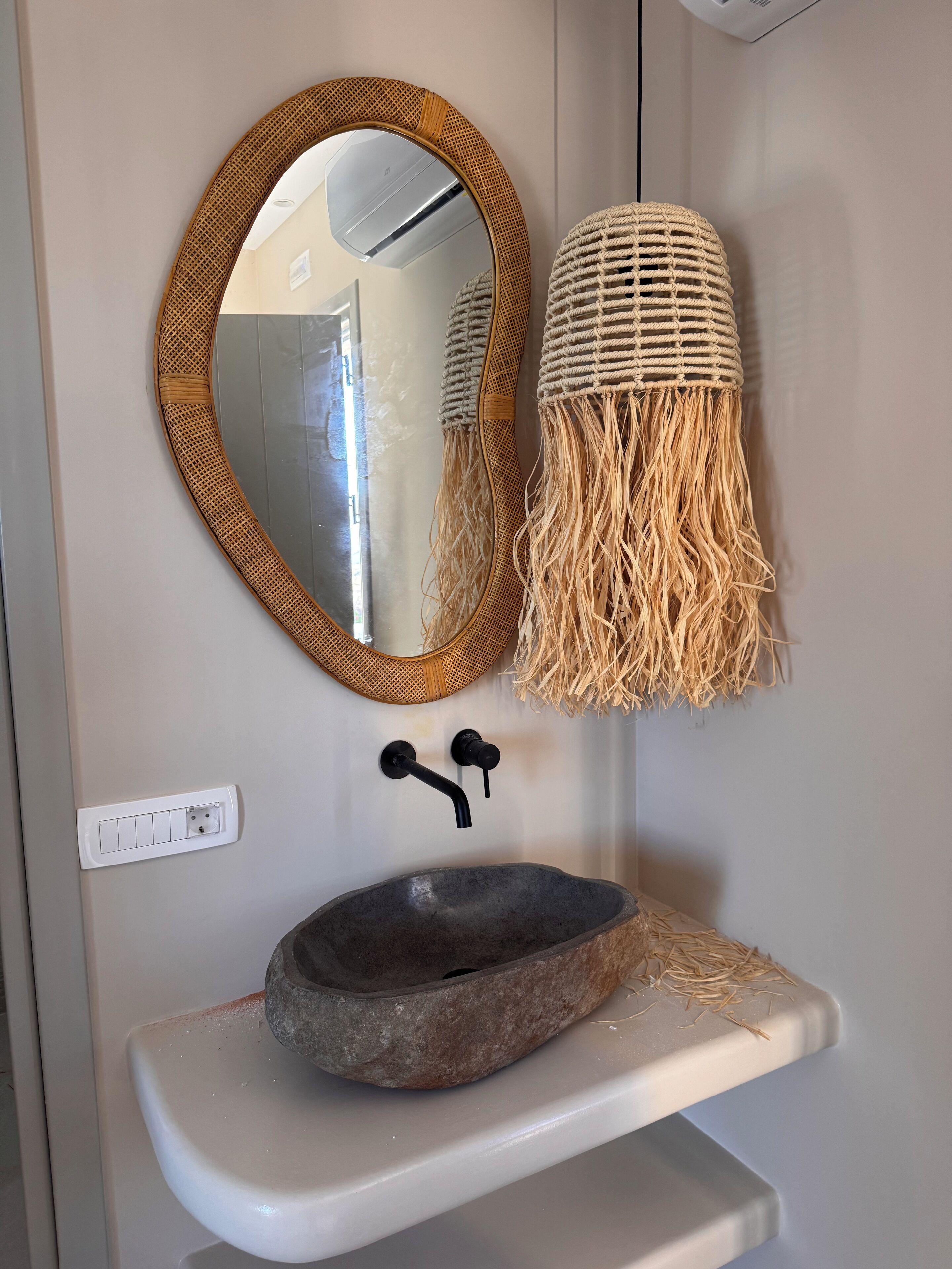 A bathroom with a round mirror, a stone sink, and a woven macrame light fixture.