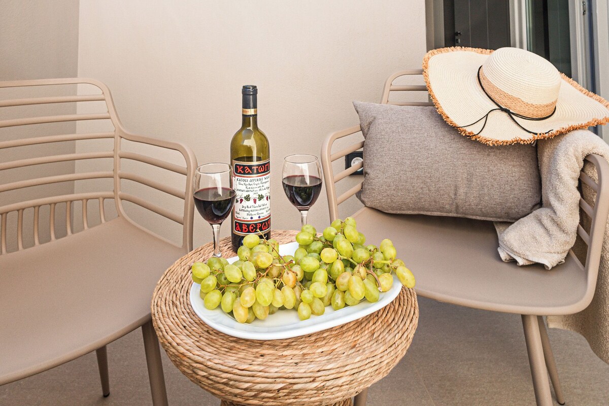 A wicker table with a bottle of wine, two glasses, and a plate of grapes.