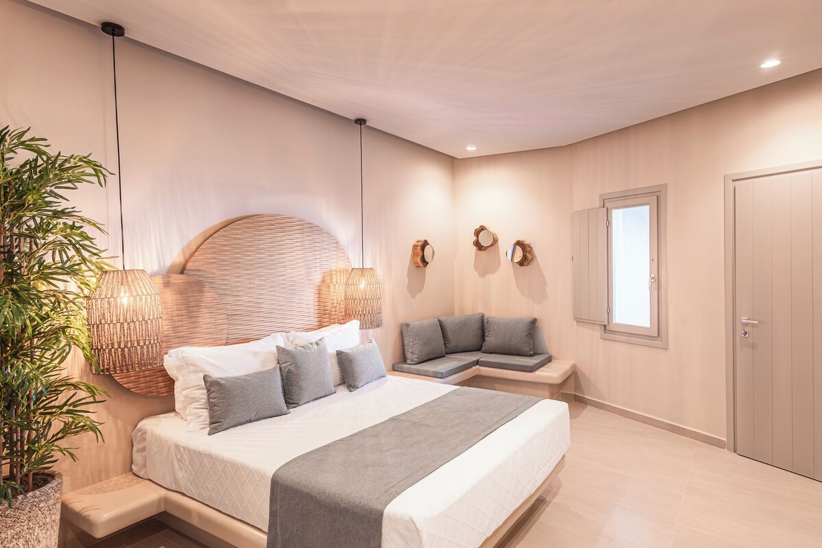 Ein Schlafzimmer mit einem Bett, Nachttischen, einer Bank, einer Topfpflanze und einer Tür.