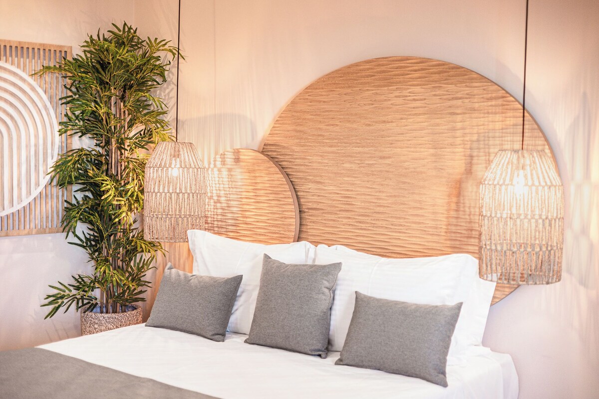 A bedroom with a large bed, a potted plant, and two hanging lamps.