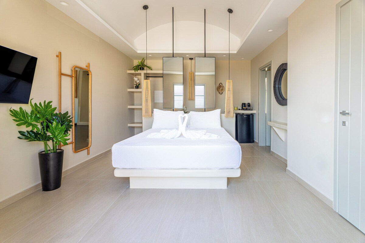 A modern bedroom with a large bed, a TV, a mirror, and a potted plant.
