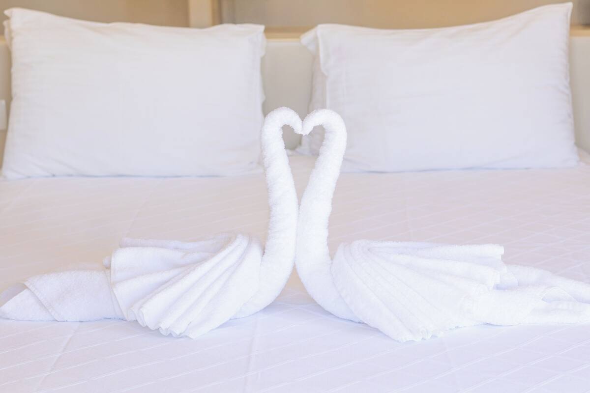A bed with white pillows and two towels arranged in a heart shape.