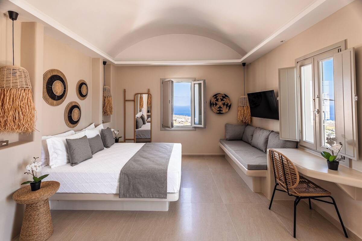 A bedroom with a bed, a desk, a chair, a TV, and a view of the sea.
