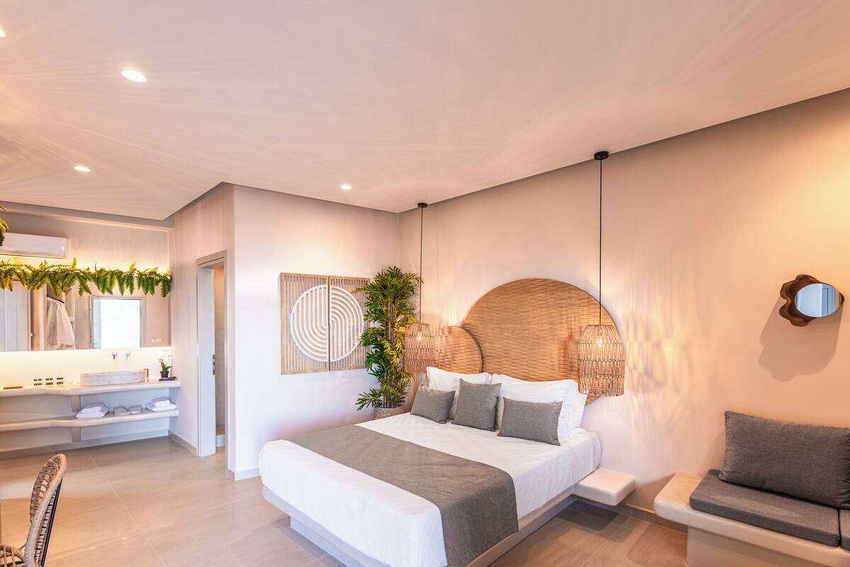 A modern bedroom with a large bed, bedside tables, a built-in bench, and a wall-mounted lamp.