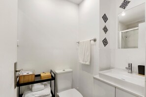 Une salle de bain moderne équipée de toilettes, d’un lavabo et d’une douche. On y trouve un porte-serviettes avec une serviette et une boîte en bois.