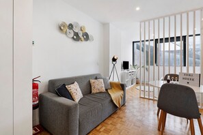 Un salon moderne avec un canapé gris, une petite table, un fauteuil et un élément décoratif mural.