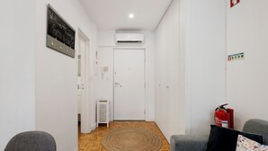 Ein Flur mit einer weißen Tür, einem Feuerlöscher, einem kleinen weißen Tisch und einem grauen Sofa.