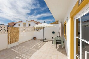 Un patio couvert avec une table et des chaises, une plante en pot et un parasol blanc.