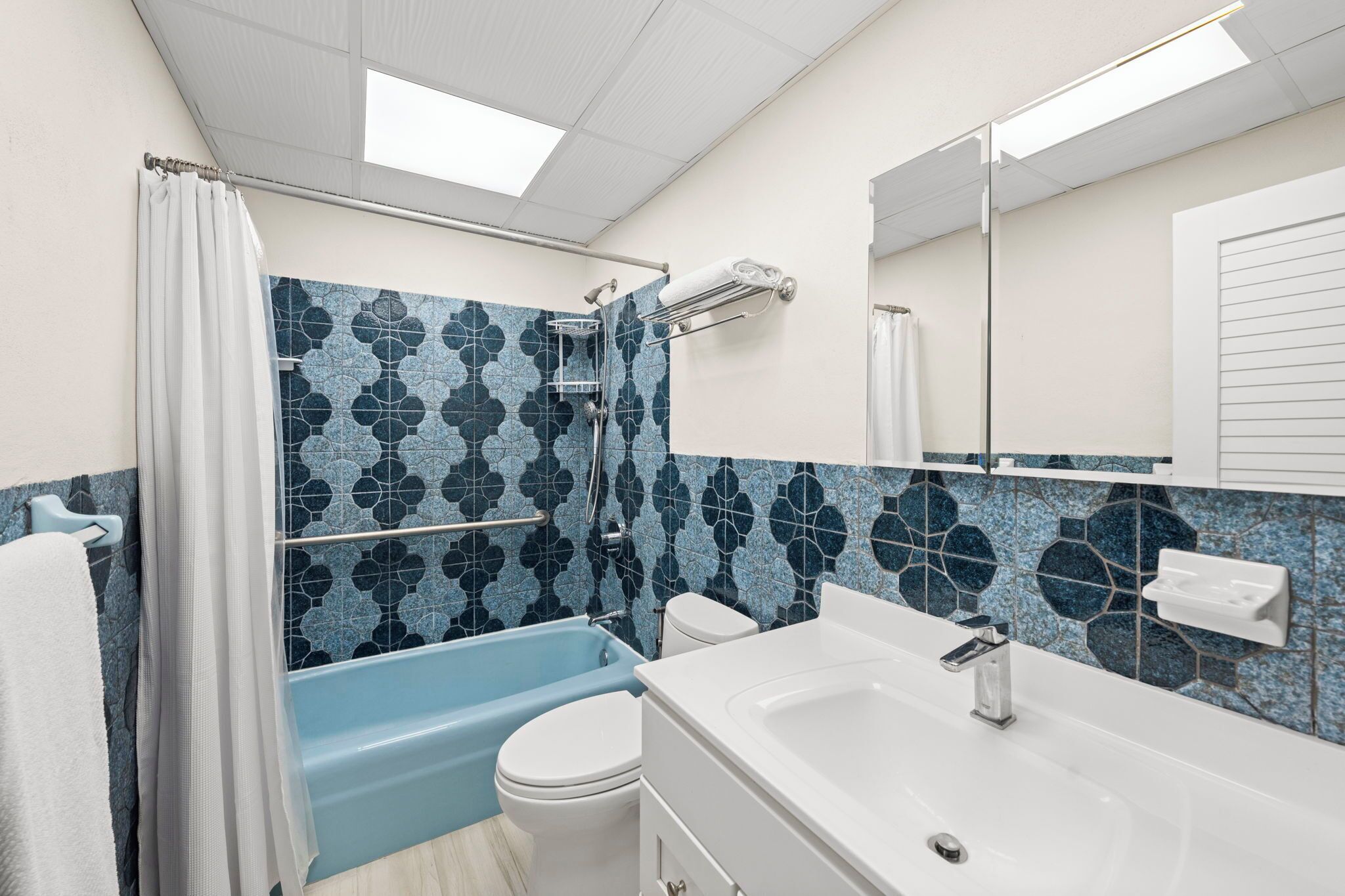 Een badkamer met een douche in blauw en wit tegels, een wit toilet en een witte wastafel met een spiegel erboven.