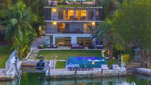 Ein modernes, zweistöckiges Haus mit Schwimmbad, umgeben von üppiger Vegetation und Palmen.
