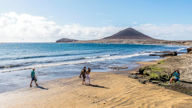 A beach with people walking and sitting, a mountain in the background, and the ocean. - Sunny Apartment with Terrace in El Médano (El Medano)