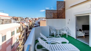 A balcony with white plastic chairs and a small table, overlooking a densely packed urban area with various buildings. - Sunny Apartment with Terrace in El Médano (El Medano)